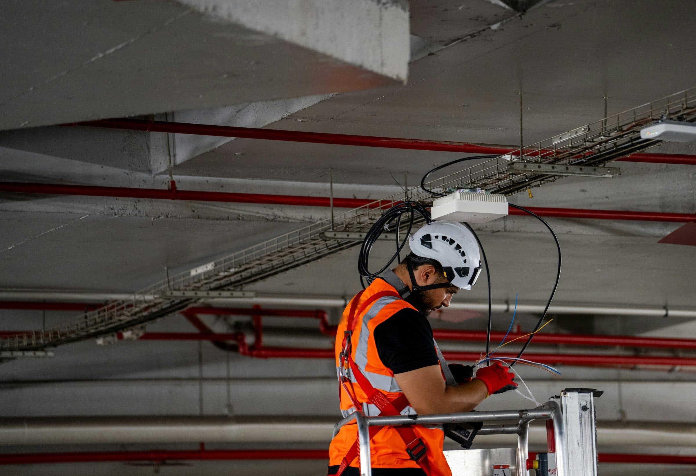 An engineer on a work platform connecting a newly fitted wireless access point under a concrete ceiling